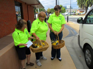 Three women wearing flurscent Murray Valley Centre shirts are pictured carry baskets of flowers. They are on their way to deliver them to customers of the Flower Power Program