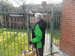 A man in a warm green and black Murray Valley Centre jacket is pictured carry baskets of flowers. He is opening a gate and on his way to deliver them to children at the Stanley Street Preschool as part of the Flowere Power program